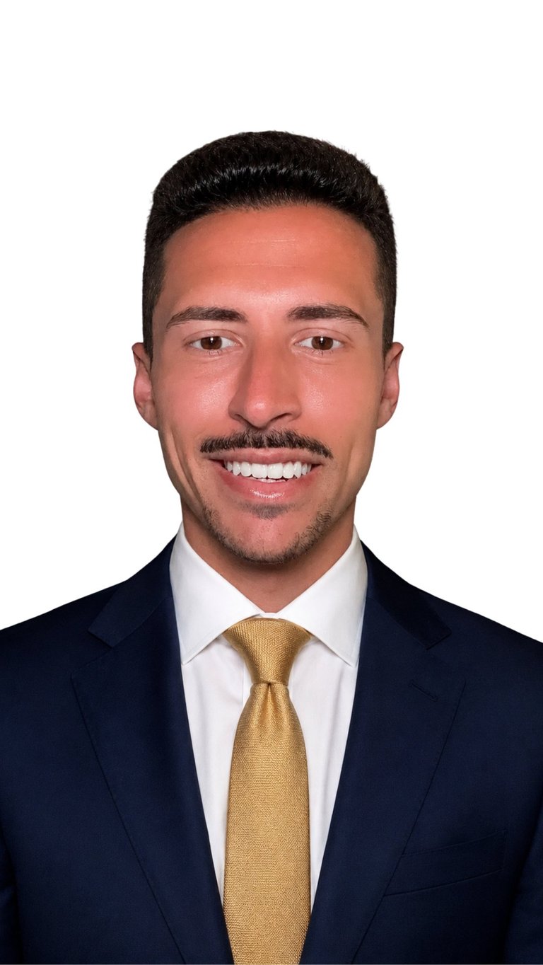 Professional headshot of a man wearing a navy blazer, white shirt, and gold tie, smiling at the camera against a white background